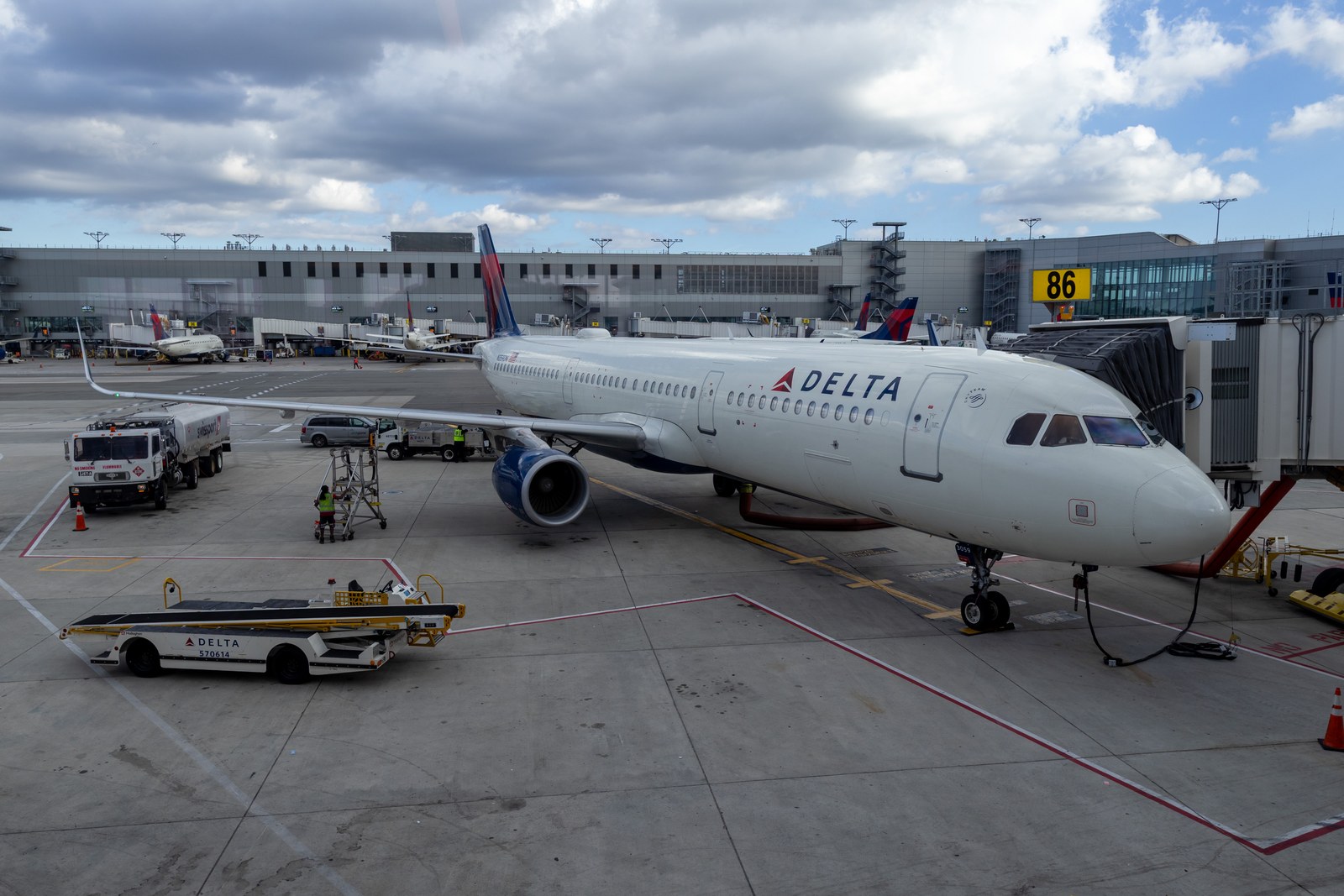 Photograph of the apron side of Terminal C in September 2025, with a Delta A321 on the jet bridge at gate 86, ground service vehicles, and the concourse facade behind